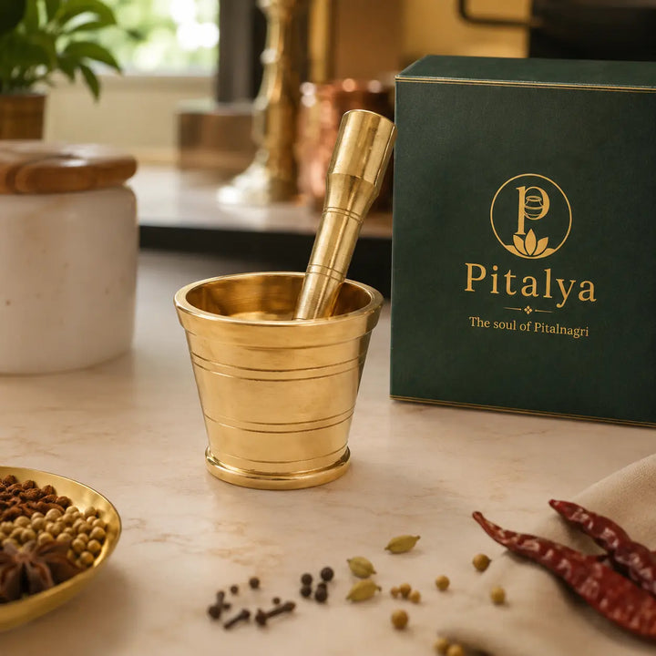 A brass mortar and pestle set with a dark green branded Pitalya gift box, styled on a marble countertop with spices and kitchen props.